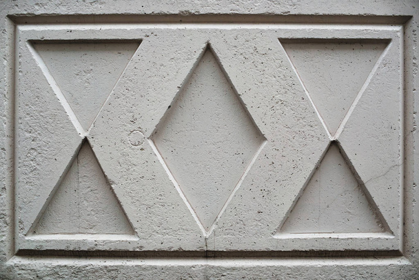 ロンバスと三角形の形をしたイメージを持つひび割れた表面を持つ古いソ連のコンクリートフェンシングクローズアップ。珍しいデザインのグランジフェンスの背景画像。アーバンホワイト耐久性のある壁. - 写真・画像