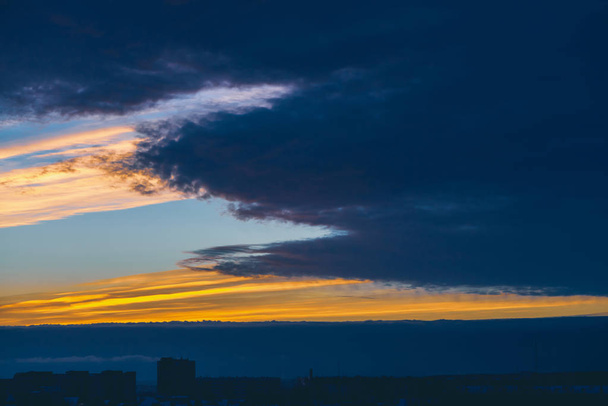 Cityscape com maravilhoso amanhecer vívido varicolored. Espantoso céu azul de nuvens acima de silhuetas escuras de telhados de construção da cidade. Fundo atmosférico de laranja nascer do sol em tempo nublado. Espaço de cópia
 - Foto, Imagem