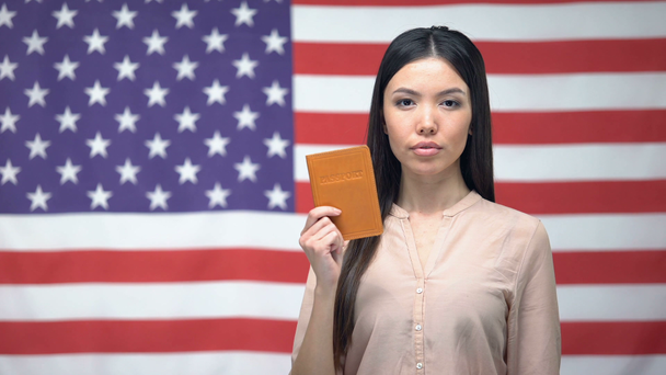 Pewnie Asian kobieta pokazując paszport przeciwko USA flaga tło, migracja - Materiał filmowy, wideo