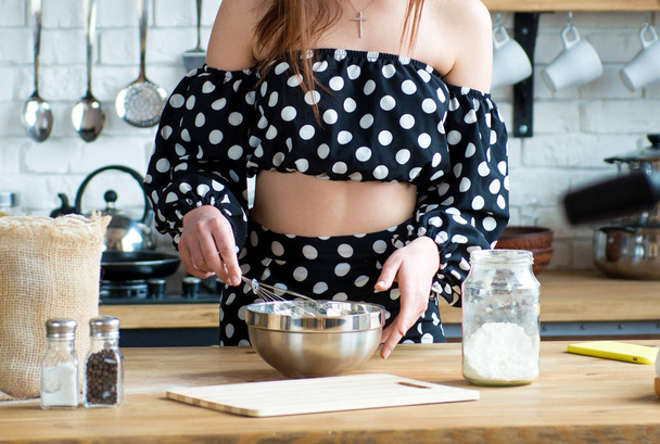 Bella ragazza bruna in un abito a pois cucina su un tavolo di legno in cucina. Primo piano della cottura - Foto, immagini