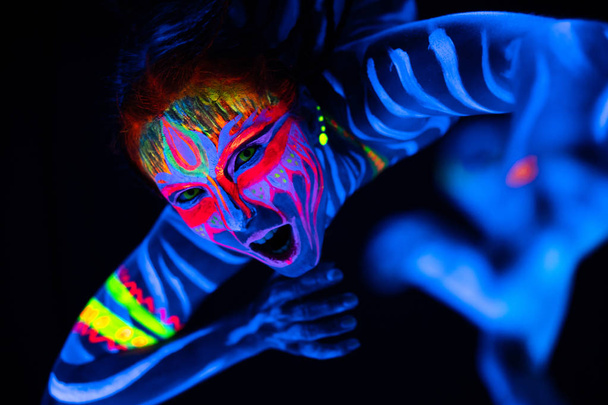 Blízký portrét divoké a šílené mladé nahé ženy v modré zářící ultrafialové barvy a žluté oční čočky. Avatarova dívka Amazonka s copánky - Fotografie, Obrázek