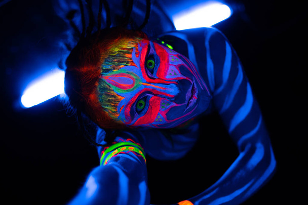 Close-up Retrato de salvaje y frenético Joven mujer desnuda bodyarted en azul brillante pintura ultravioleta y lentes de ojo amarillo. Avatar entidad amazona guerrera chica con coletas peinado
 - Foto, imagen