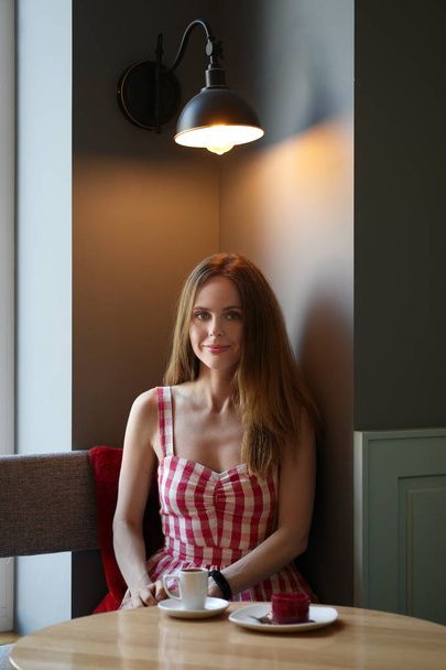 Cute girl in cafe having coffe and cake sitting in the corner by the window - Фото, зображення