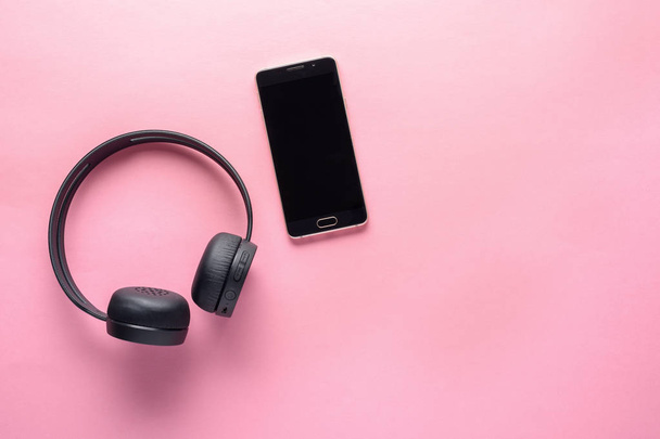 concept van gadgets voor muziekliefhebbers. draadloze koptelefoon en smartphone op roze achtergrond met kopieerruimte - Foto, afbeelding