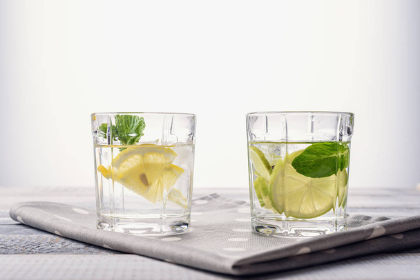 close-up glass of water with lemon, lime and mint on light gray wooden background - Foto, afbeelding