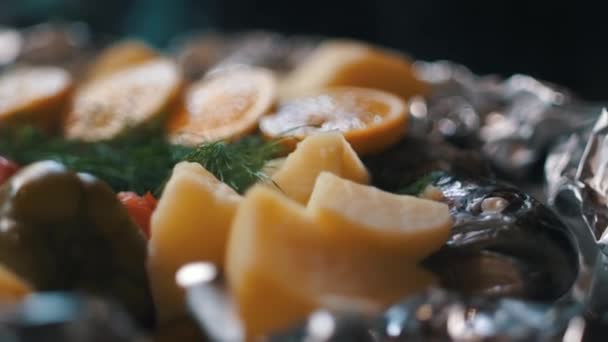 Ψημένο ψάρι με πατάτες, λαχανικά και λεμόνι, μετατρέπεται σε ένα πιάτο μπροστά από την κάμερα. - Πλάνα, βίντεο