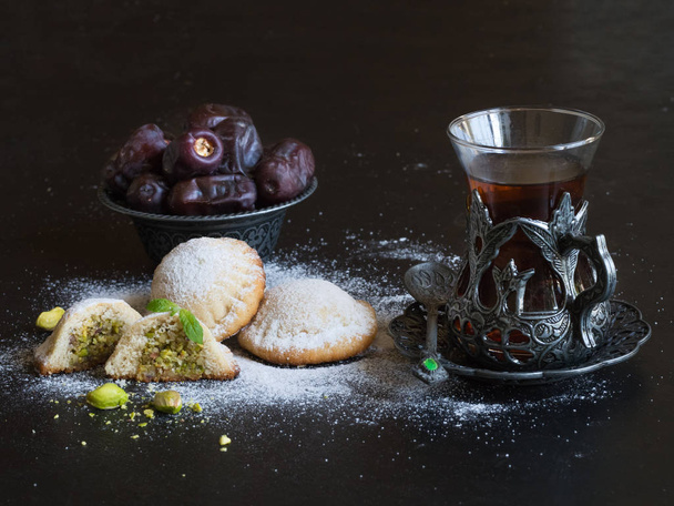 Арабское печенье Maamoul с датами и чашкой чая на черном фоне. Рамадан сладости фон
. - Фото, изображение