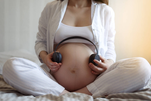 Musique pour enceinte. gros plan de la femme enceinte avec casque sans fil s'applique au ventre
 - Photo, image