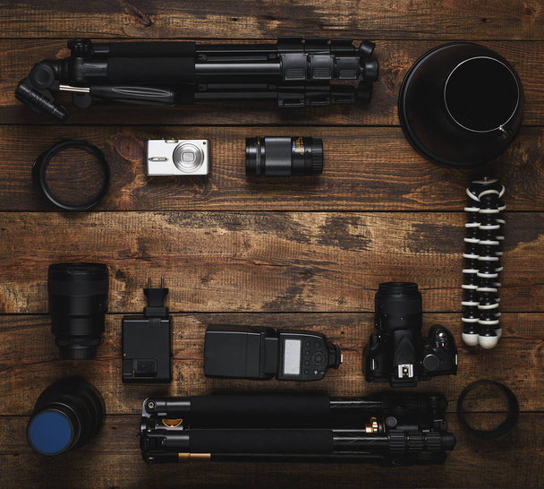 Top view of the equipment photographer, videographer, blogger traveler, with a copy of the space. DSLR, pocket camera, tripods, lenses on wooden texture background - Zdjęcie, obraz