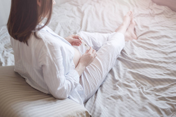 Молодая беременная женщина в постели с термометром, место для смс
 - Фото, изображение