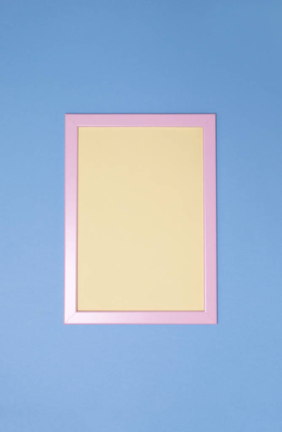 Empty pink photoframe with yellow paper inside on blue background. Copy space. Top view. Vertical. - Φωτογραφία, εικόνα