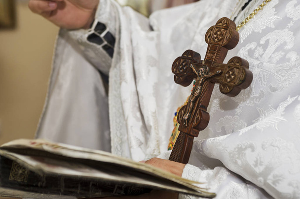 Sacerdote macho segura em suas mãos cruz de madeira sobre a Bíblia sagrada e orando. Conceito cristão
 - Foto, Imagem
