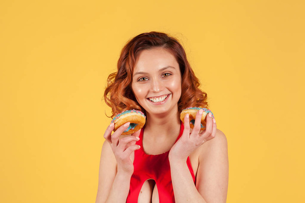 meisje in rode badpak Holding donuts met blauwe glazuur op gele achtergrond - Foto, afbeelding