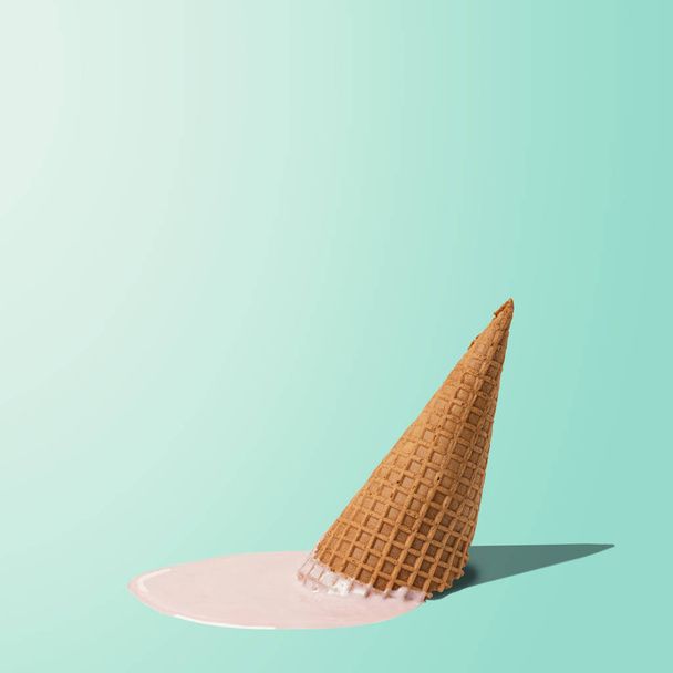 Melted ice cream with ice cream cone on pastel blue background. Minimal summer food concept.  - Foto, afbeelding