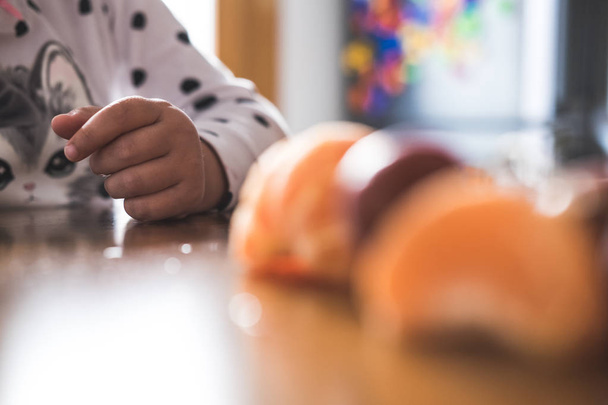 Рука ребенка манипулирует различными фруктами на деревянном столе
 - Фото, изображение