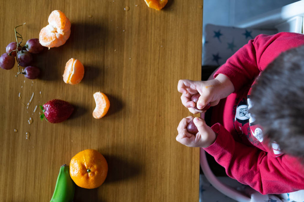 木製のテーブルの上に異なる果物を操作する赤ちゃんの手 - 写真・画像
