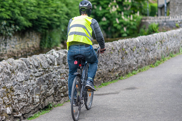 Ένας αρσενικός ποδηλάτης καβαλάει ένα ποδήλατο σε πλήρη εξοπλισμό ασφαλείας-κράνος, υψηλή ορατότητα μπουφάν, Φώτα ποδηλάτου - Φωτογραφία, εικόνα