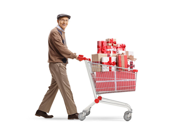 Full length shot of an elderly man with a shopping cart full of presents smiling at the camera isolated on white background - Fotoğraf, Görsel