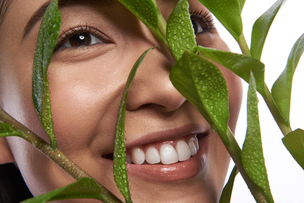 Gesicht einer lächelnden Asiatin hinter den grünen Blättern - Foto, Bild
