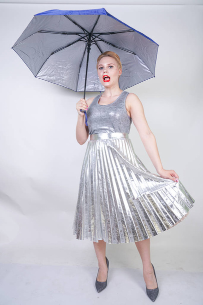cute chubby short hair girl in a modern city metallic silver dress holding an umbrella and posing on a white background in the Studio alone - Фото, изображение