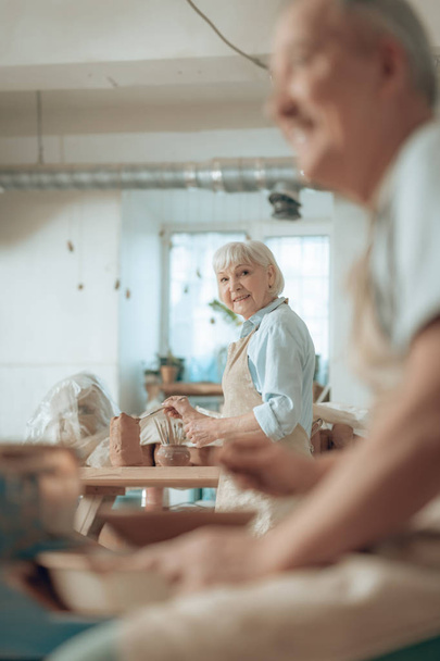 Waist up of smiling elderly craftswoman painting earthenware in potters studio - Fotografie, Obrázek