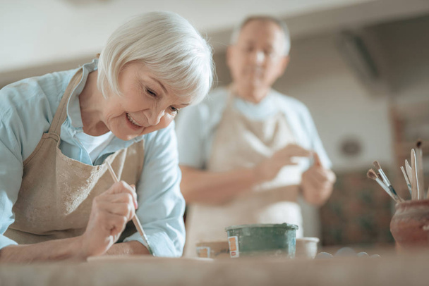 Cropped photo of elderly craftswoman painting decorative plate in workshop - Fotografie, Obrázek