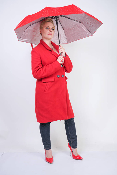 cute short hair chubby girl in a modern city wool coat holding a red umbrella and posing on a white background in the Studio alone - Fotó, kép