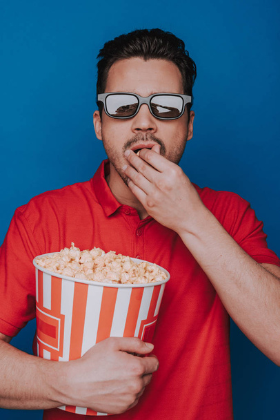 Waist up of Caucasian man holding popcorn bucket on blue background - Foto, Imagen
