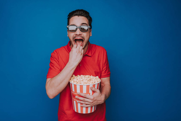 Caucasian man with opened mouth holding popcorn bucket on blue background - Фото, зображення