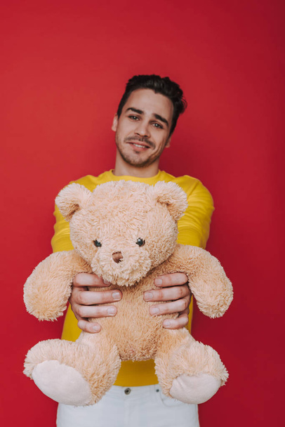 Waist up of smiling unshaven man showing teddy bear for camera - Photo, image
