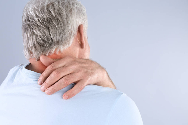 Senior man scratching neck on grey background, space for text. Allergy symptom - Foto, afbeelding