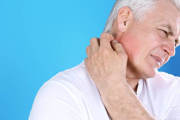 Senior man scratching neck on color background, closeup with space for text. Allergy symptom - Foto, Bild