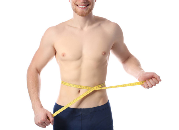 Young man with measuring tape showing his slim body on white background, closeup - Fotó, kép