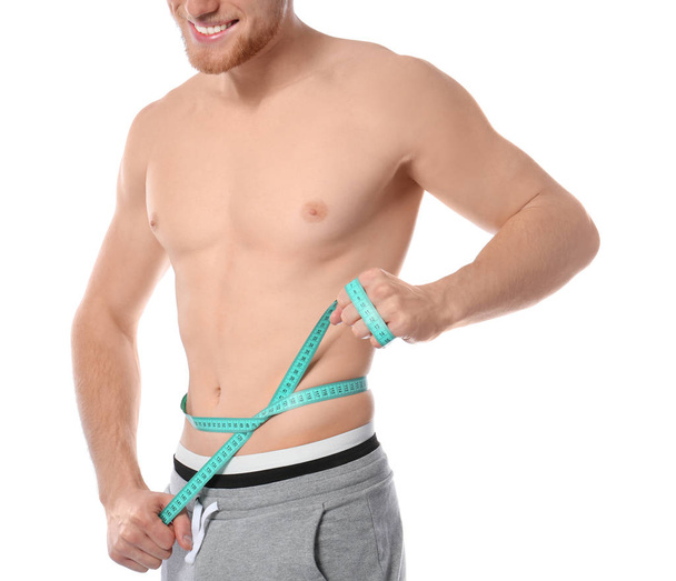 Young man with measuring tape showing his slim body on white background, closeup - 写真・画像