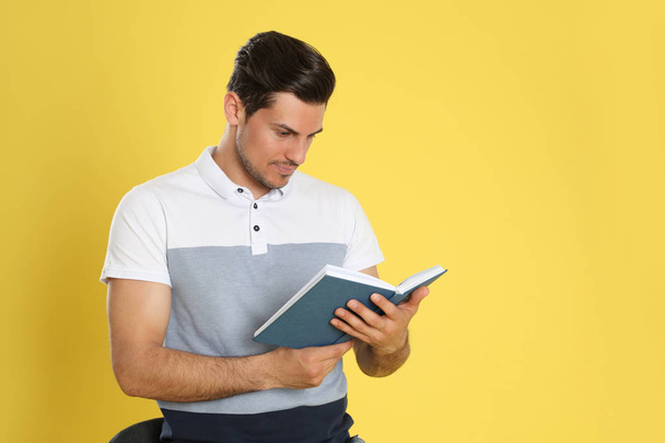 Handsome man reading book on color background, space for text - Fotó, kép