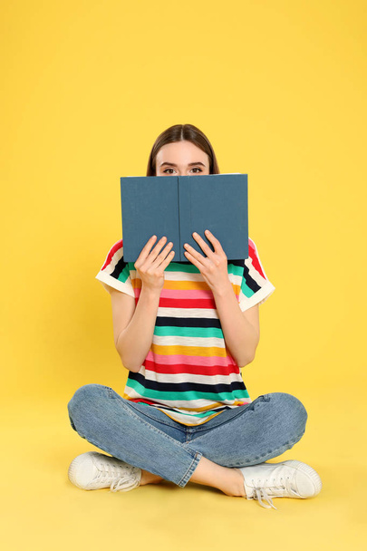 Young woman reading book on color background, space for text - Foto, afbeelding