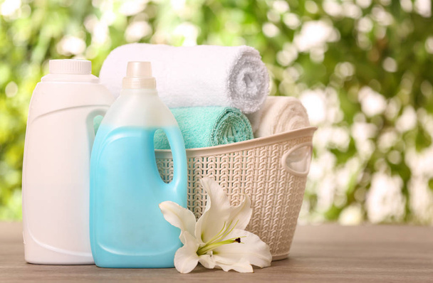 saubere Handtücher im Korb mit Lilie und Reinigungsmitteln auf dem Tisch vor verschwommenem Hintergrund. Raum für Text - Foto, Bild