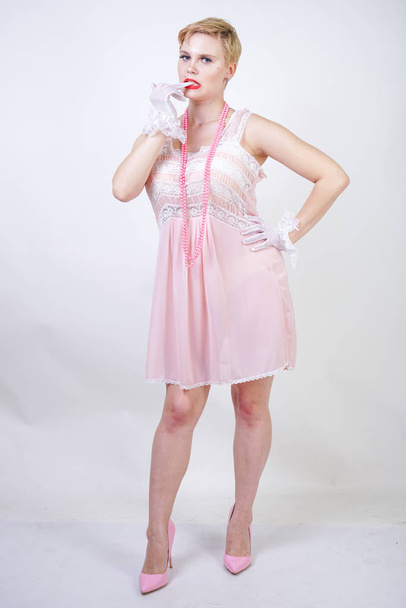 Romantická a velikostní dívka s krátkými blond vlasy v růžových krajkových šatech, bílé tenké průhledné rukavice a perlové kuličky na bílém pozadí samotného studia - Fotografie, Obrázek