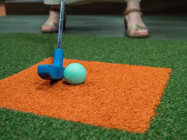 putter blu sul tappeto erboso allineato accanto alla palla da golf verde sul campo da golf in miniatura con la donna che gioca
 - Foto, immagini