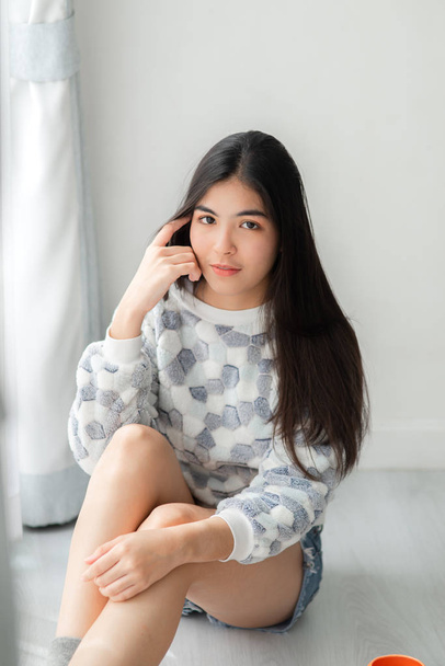 Thoughtfull Asian teenager sitting on floor near window with ora - Fotoğraf, Görsel