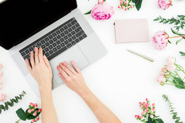 Γυναίκα που δακτυλογραφεί στο λάπτοπ. Χώρος εργασίας με γυναικεία χέρια, φορητό υπολογιστή και ροζ λουλούδια σε λευκό φόντο. Κορυφαία προβολή. "Επίπεδη". Αντιγραφή χώρου - Φωτογραφία, εικόνα