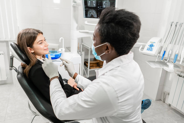 Arzt behandelt Zähne. junger afrikanischer Zahnarzt mit einer Patientin. Frau im Zahnarztstuhl in der Zahnklinik. Medizin, Gesundheit, Stomatologie-Konzept. Zahnarzt behandelt einen Patienten. - Foto, Bild