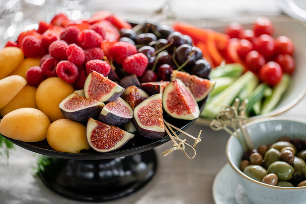 Table with cold snacks and tableware. Fresh Fruit platter on banquet table at business or wedding event venue. Raspberry, strawberry, cherry, Fig, apricote. Self service. - Фото, зображення