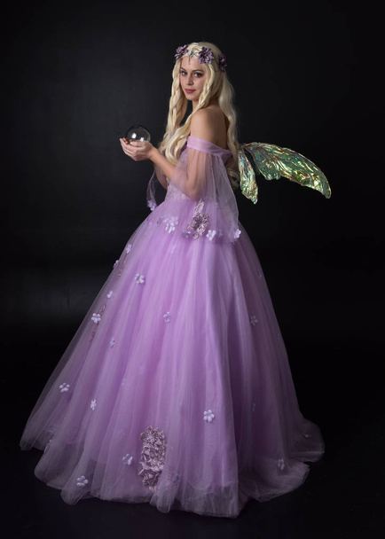 портрет блондинки в фентезі фея, натхненний костюм, довгий фіолетовий м'яч з казковими крилами, сидить позу на темному студійному фоні
. - Фото, зображення