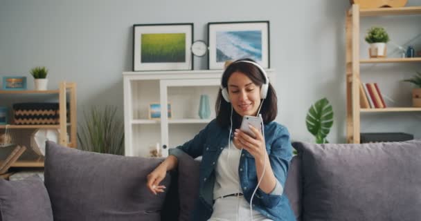 Happy relaxed girl listening to music in headphones holding smartphone - Video