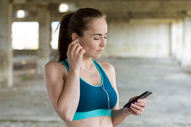 Young sportswoman listening music in earphones on smartphone - Фото, изображение