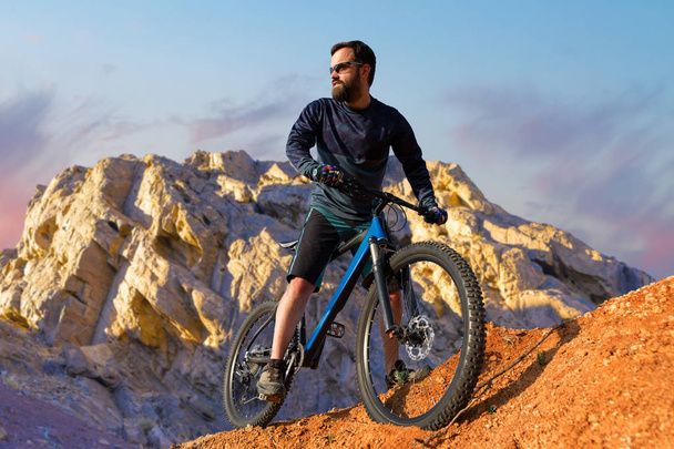 Cyclist in shorts and jersey on a modern carbon hardtail bike with an air suspension fork standing on a cliff against the background of fresh green summer forest - Photo, Image