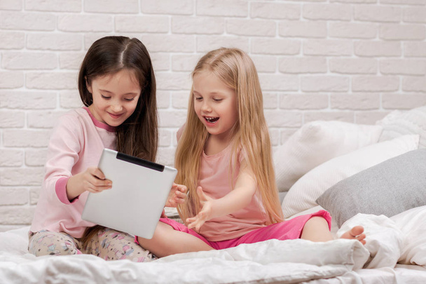two cute children girls use digital tablet in bed. - Foto, afbeelding