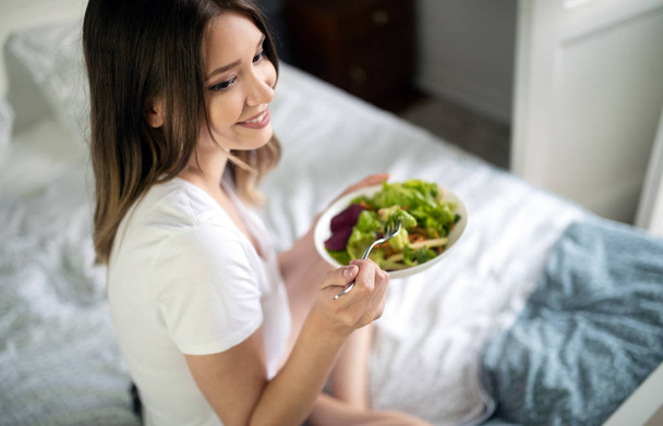 Woman eating healthy salad after working out at home - Foto, Bild