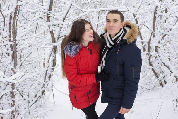 The guy and the girl have a rest in the winter woods. Husband and wife in the snow. Young couple walking in winter park - Zdjęcie, obraz